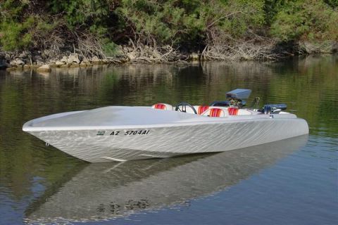 1991 Ford Bronco - A silver boat with a distinctive textured hull is seen on the water, a red and white striped interior and a visible engine.