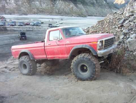 2000 Ford F-450 - Modified red pickup truck navigates a rocky, off-road environment with other vehicles visible.
