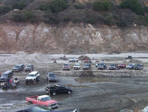 2000 Ford F-450 - A variety of trucks, SUVs, and ATVs are gathered in a sandy, outdoor recreational area with a rocky hillside in the background.