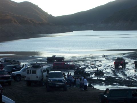 2000 Ford F-450 - A group of off-road vehicles are gathered by a lake on a sunny day.