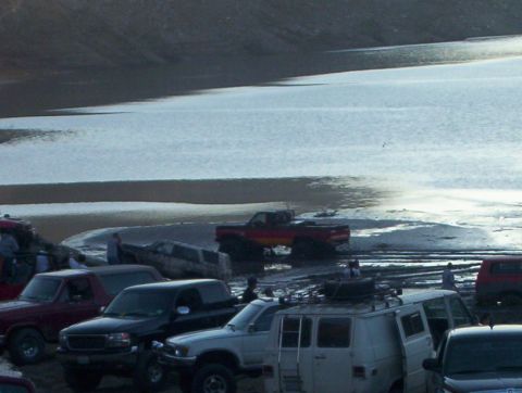2000 Ford F-450 - Multiple vehicles are gathered on a muddy shore next to a large expanse of water.