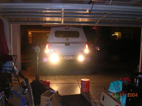 2004 Ford F-250 - The rear of a pickup truck with a camper shell is visible in a garage, with its reverse lights illuminated.