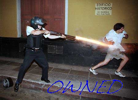 1986 Ford Bronco - Man fires shotgun at another man in a street scene with building in background.