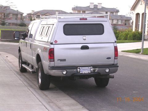 2004 Ford F-250 - Silver 2004 Ford F-250 pickup truck with a camper shell parked on a residential street.