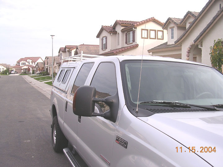 Silver Ford F-250 crew cab with tow mirror and camper shell seen from the front fender