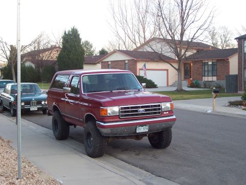1991 Ford Bronco - This lifted 1991 Ford Bronco is parked on a residential street next to another car.