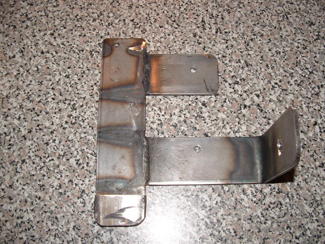 Welded metal bracket with holes, resting on speckled surface