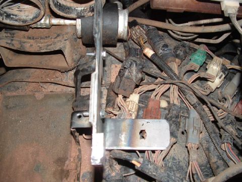 1990 Ford Bronco - A bare fabricated steel bracket bolted vertically into a dusty engine bay, its heat-tinted flat foot drilled with a slot and hole and a rub…