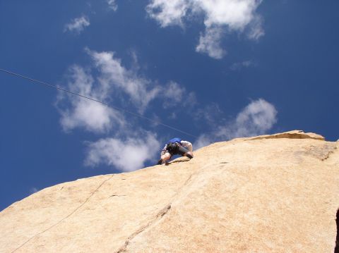 1990 Ford Bronco - A person climbs a rock face, with a rope and a clear blue sky above.
