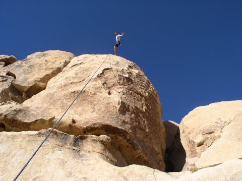 1990 Ford Bronco - A climber stands atop a rock formation against a clear blue sky.