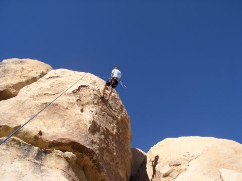 1990 Ford Bronco - A person rappels down a large rock formation under a clear blue sky.