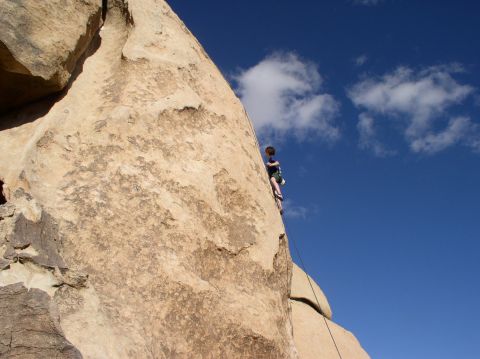 1990 Ford Bronco - A lone climber scales a massive rock formation against a bright blue sky.
