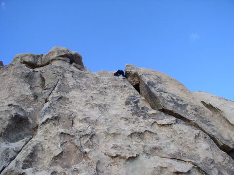 1990 Ford Bronco - A lone climber scales a massive rock formation against a bright blue sky, with a website watermark at the bottom.