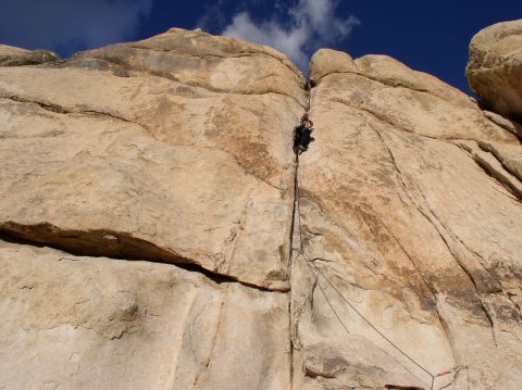 1990 Ford Bronco - A lone climber scales a challenging rock face, suspended by ropes against a backdrop of stone and sky.