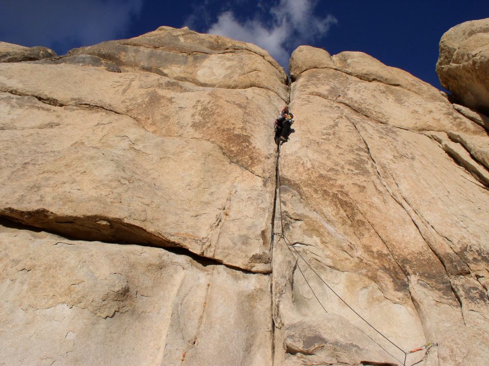 Rock climber ascending a narrow crack on a large rock face under a blue sky