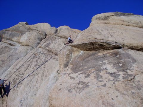 1990 Ford Bronco - People are rock climbing on a large rock formation under a clear blue sky.