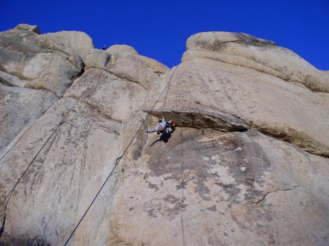 1990 Ford Bronco - Two individuals are engaged in rock climbing on a steep, sunlit cliff face with ropes and climbing gear visible.