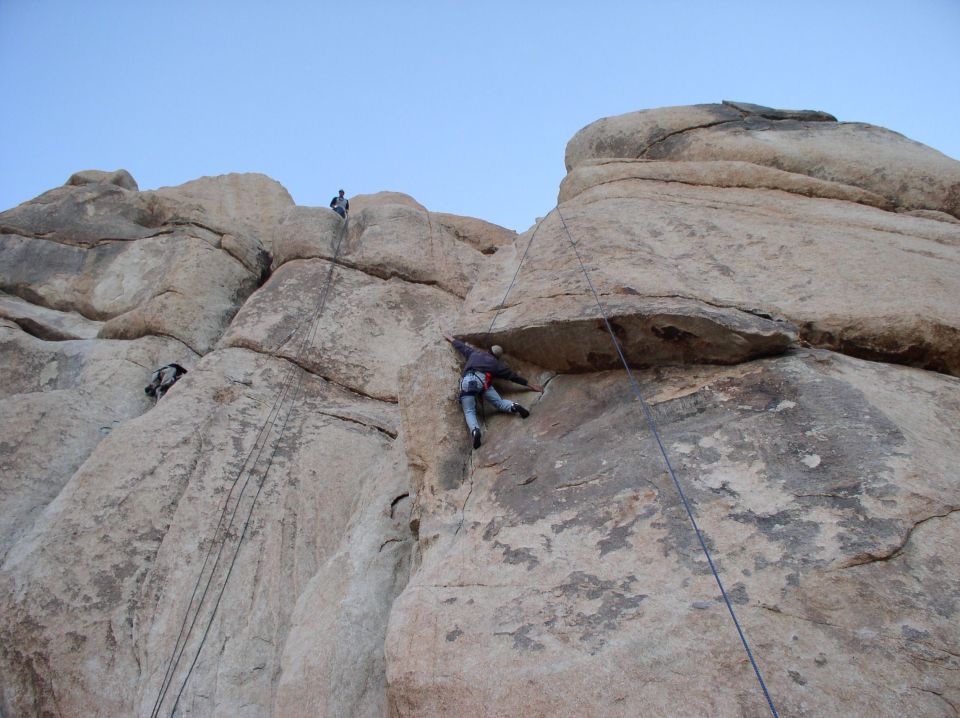 People climbing a large rock formation with ropes and harnesses