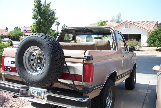 Tan Ford Bronco with top removed, rear spare tire carrier and Arizona plate 743-HTR, parked in a driveway