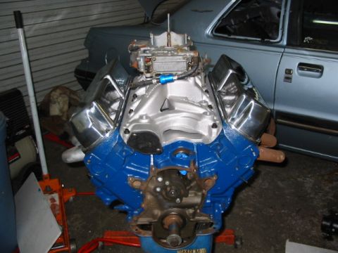 1985 Ford Crown Victoria LTD - A rebuilt V8 engine sits on an engine stand in front of a car.