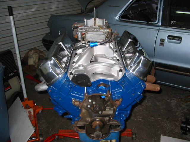 Blue V8 engine with chrome valve covers and a carburetor on a stand