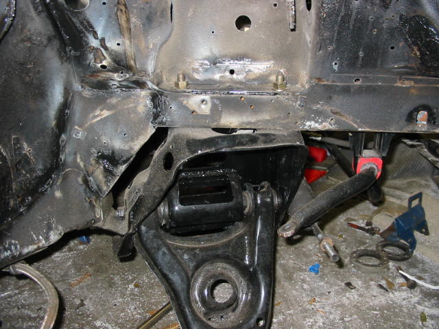 Black lower control arm and stripped front frame of a car under restoration in a garage