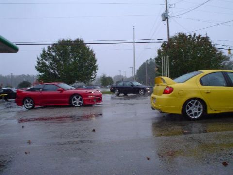 1996 Ford Probe - A red 1996 Ford Probe is parked on a wet asphalt lot next to a yellow Dodge Neon.