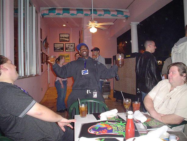 People gathered at tables inside a restaurant with pink walls and a ceiling fan