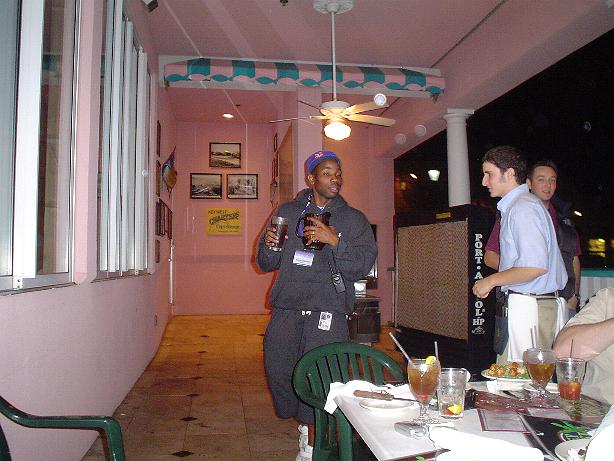 Three men stand near a table with drinks and food at an outdoor restaurant