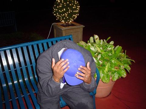 1996 Ford Probe - A person sits on a blue bench, head down and hands covering their face, next to a potted plant and a decorated tree.