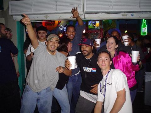1996 Ford Probe - People celebrating and holding drinks inside a dimly lit bar with neon signs.