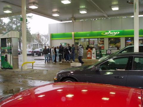1996 Ford Probe - A group of people gather at a gas station under a covered canopy, with several vehicles visible.
