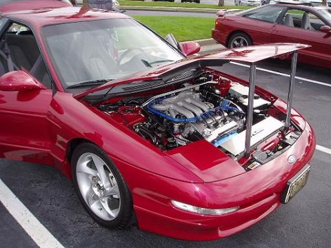 1996 Ford Probe - A red 1996 Ford Probe is displayed with its hood open, revealing the engine, while another similar car is parked nearby.