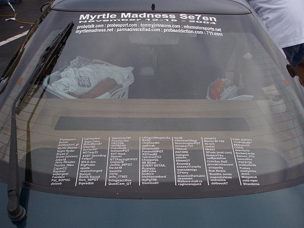 Car rear window with multiple stickers, including 'Myrtle Madness Se7en' and many names