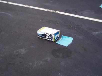 1996 Ford Probe - A box with a car wheel graphic sits on asphalt near a white line.
