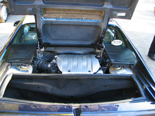 Engine bay of a dark-colored car with the hood open. Text on sticker reads 'NO DUES'