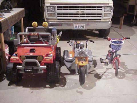 1989 Ford Bronco - Three toy vehicles are parked in a garage in front of a larger vehicle.