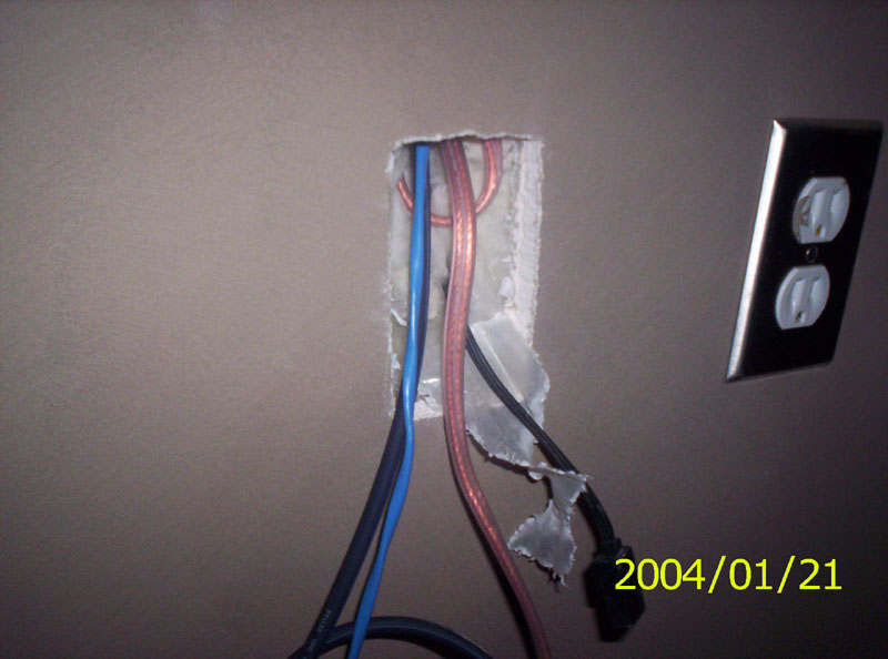 Exposed wires emerging from a wall opening next to a double electrical outlet