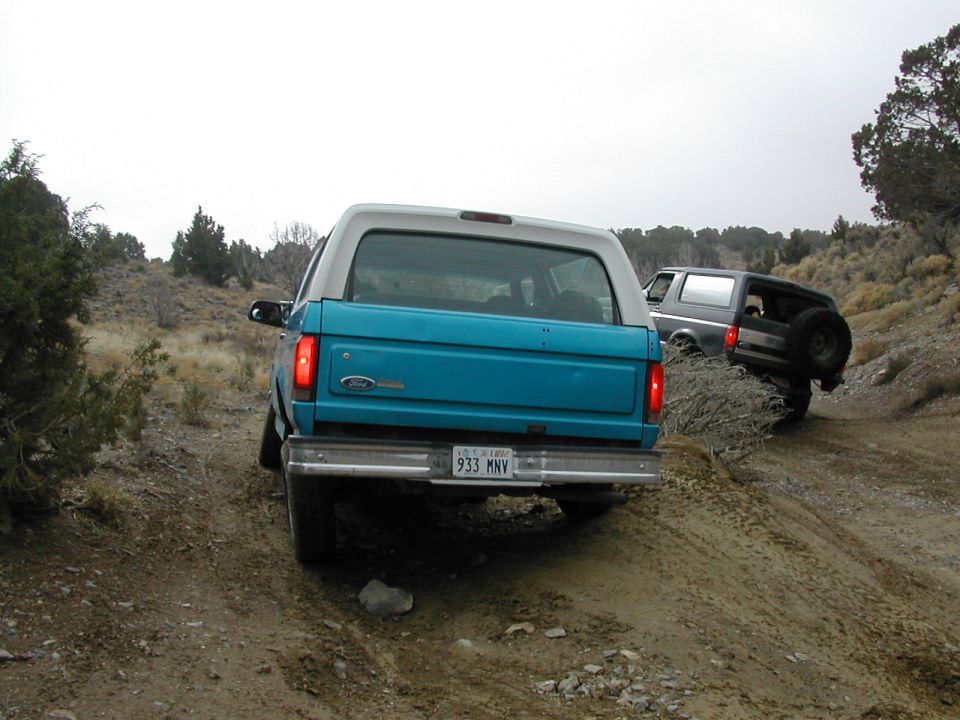 Rear of teal Ford SUV on dirt off-road trail with dark SUV ahead