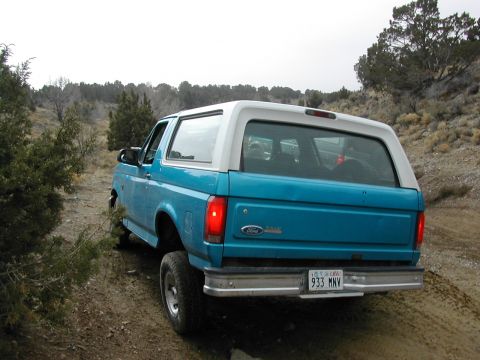 1994 Ford Bronco - This 1994 Ford Bronco is seen from the rear, driving on a dirt road in a dry, arid landscape.