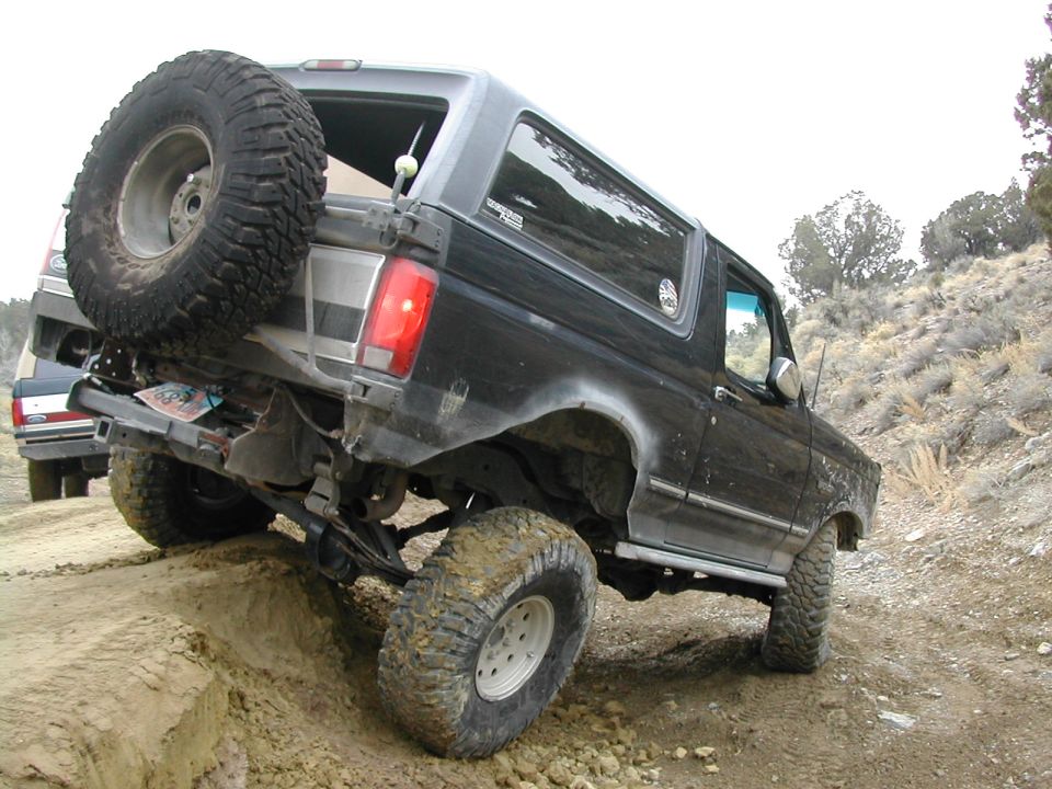 Black 1994 Ford Bronco climbing a dirt hill with a spare tire on the back
