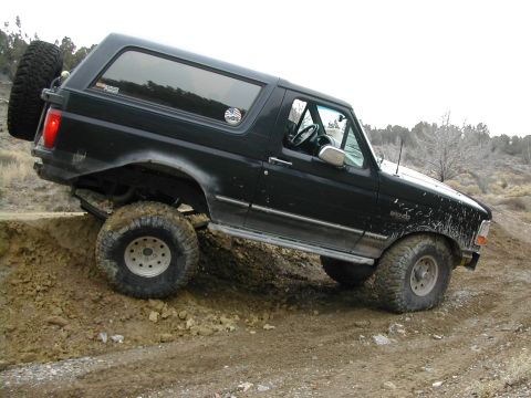 1994 Ford Bronco - A black Ford Bronco navigates a steep dirt embankment off-road.