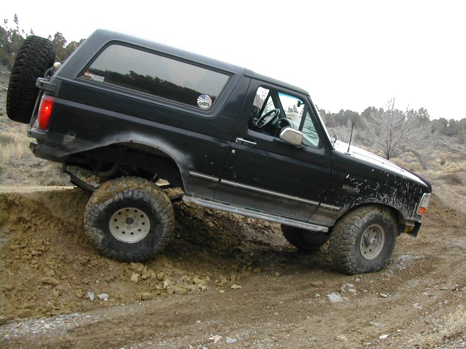 Black Ford Bronco with a spare tire on the rear, angled on a dirt incline
