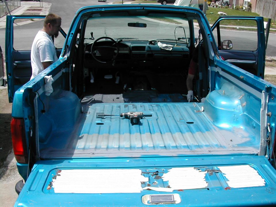 Teal Ford Bronco, top off and interior stripped, tailgate down with a drill on the bare floor during bedliner prep