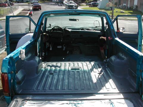 1994 Ford Bronco - Teal pickup truck interior and bed are shown with doors open, revealing the dashboard and steering wheel.