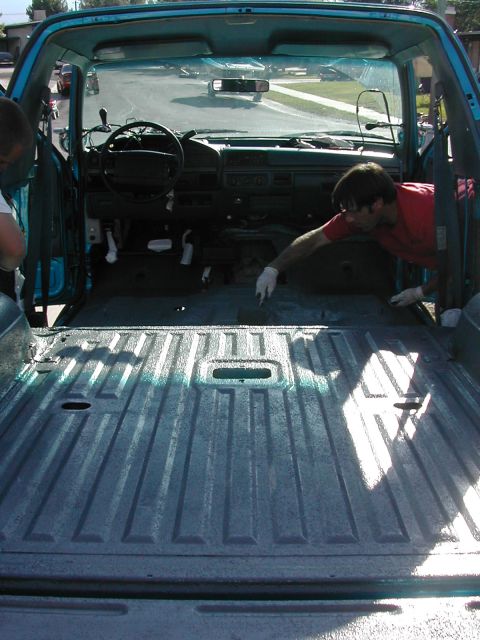 1994 Ford Bronco - Two people work on the interior and bed of a teal pickup truck.
