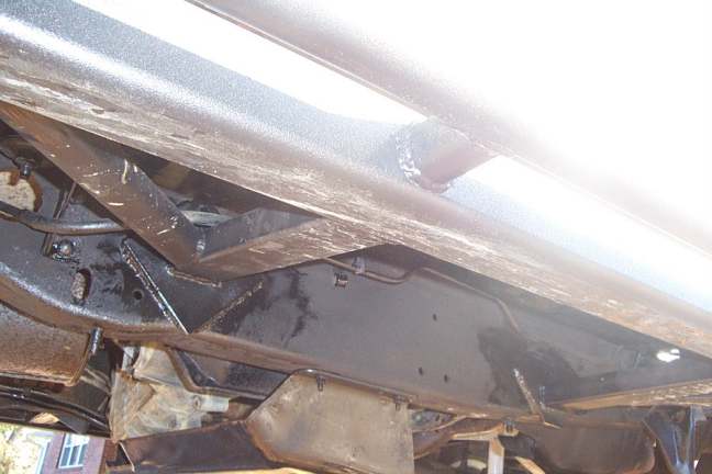 Underbody view of a black-painted frame rail, crossmember and floor pan