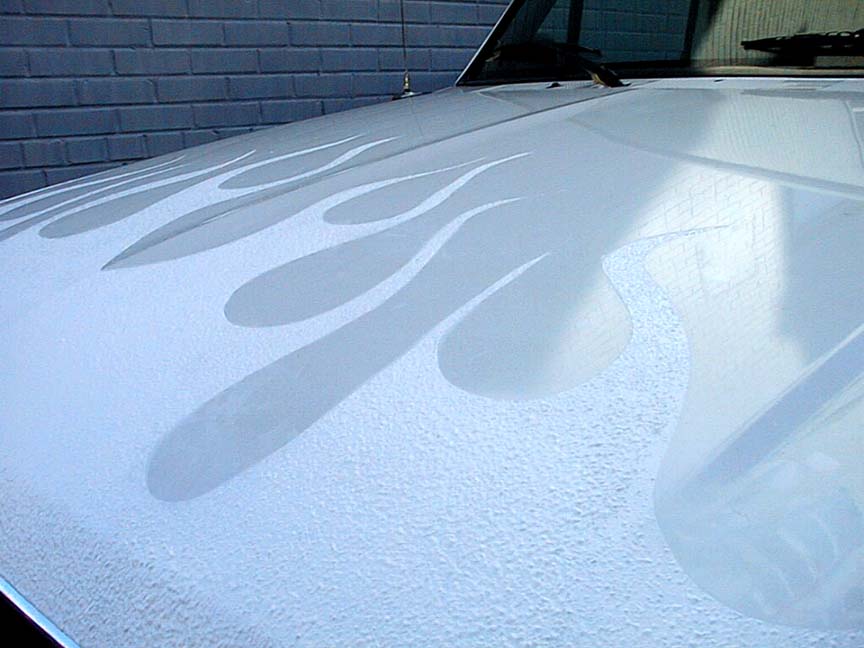 White car hood painted with ghost flames against a painted brick garage wall