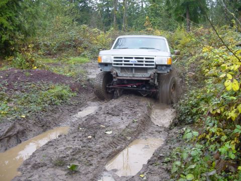 1987 Ford Bronco - This 1987 Ford Bronco is navigating a challenging muddy path in a wooded area.