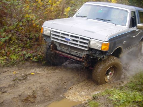 1987 Ford Bronco - A 1987 Ford Bronco navigates a muddy trail, kicking up water and dirt.